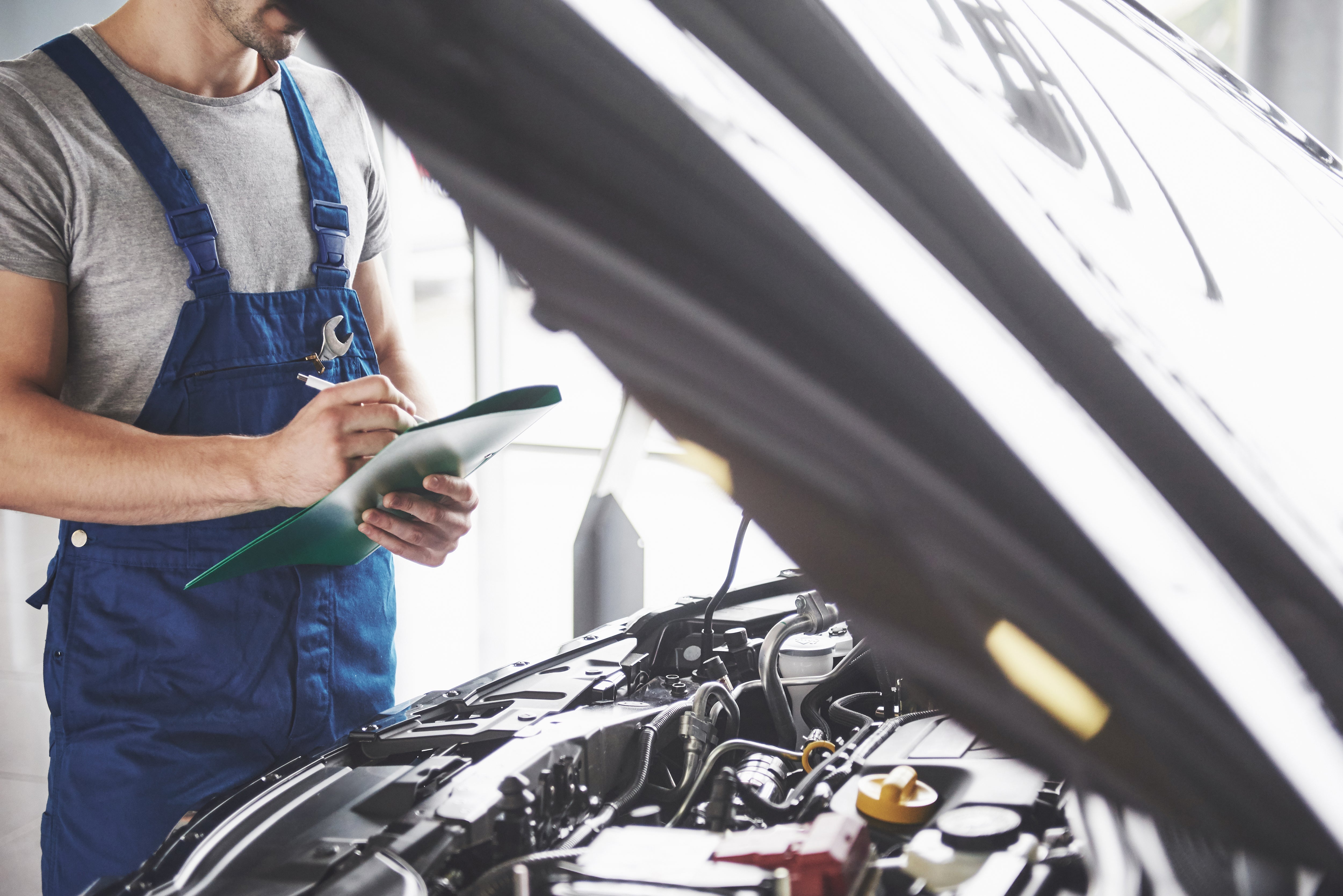 Here’s a concise, descriptive alt text for that image:  "Mechanic inspecting a car during an MOT test to check brakes, lights, and tyres for road safety compliance